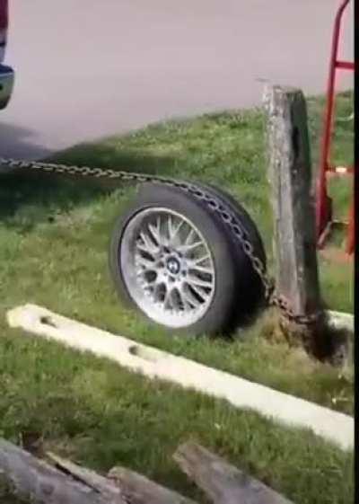 Pulling a post from the ground with a chain wrapped around a car wheel