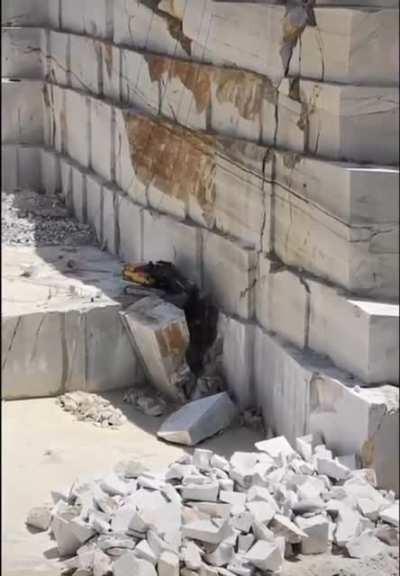 An excavator in a quarry removing an enormous slab of marble