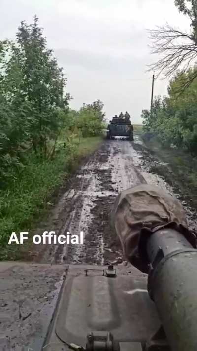 A pair of Ukrainian 2S1 Gvozdika 122mm self-propelled howitzers drives down a muddy forest track after rain.