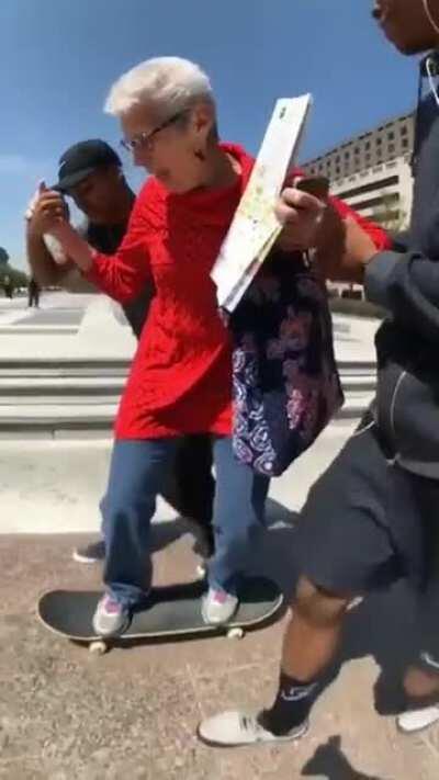 Two young skaters help an older woman skateboard for the first time and she's stoked