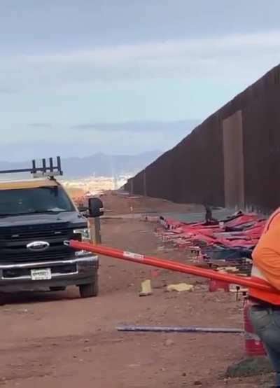 Illegal immigrant scales the wall at the US-Mexico border while workers are building it