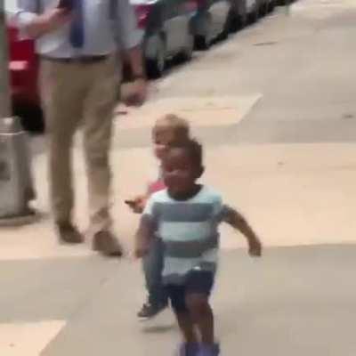 Two toddler besties run towards each other and hug on the street