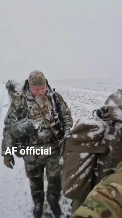 Ukrainian troops march through falling snow looking tired but still able to raise a smile.