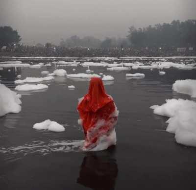 Woman praying in Yamuna river as toxic foam floats over her