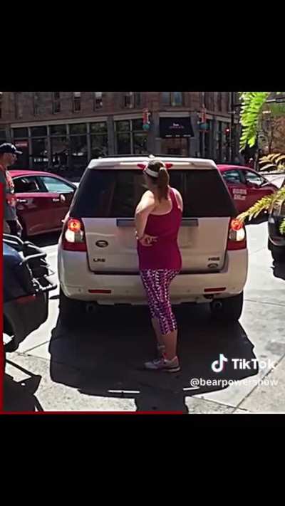 A woman believing that she can reserve a spot on a public street, blocks a vehicle from parking