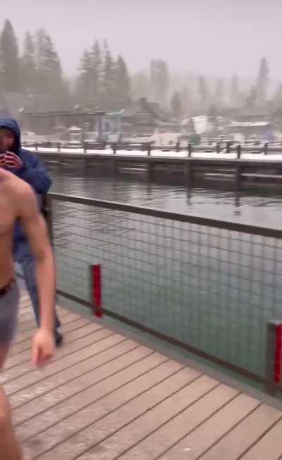 Guy tries to jump over a barrier into the water in the snow 