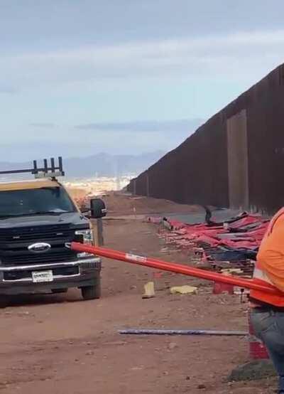 Man climbs the US-Mexico border while people are working on it