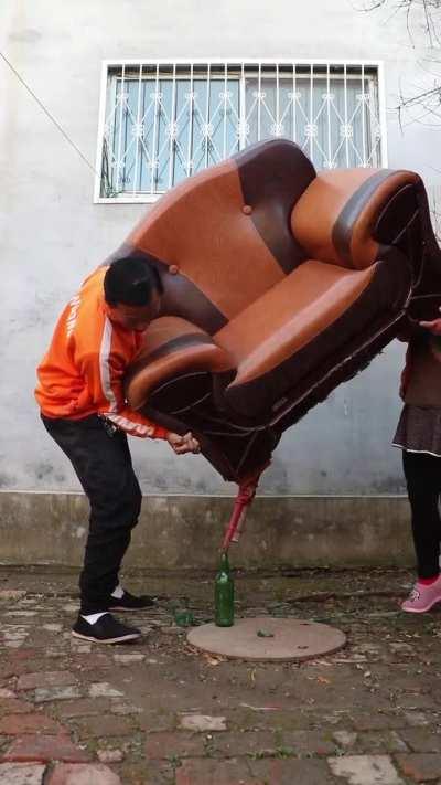 Man balances a whole armchair on a singular beer bottle