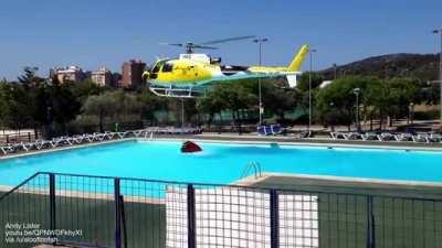 Forest fire helicopter uses a swimming pool to load water into a specialised bucket with release valve for aerial firefighting