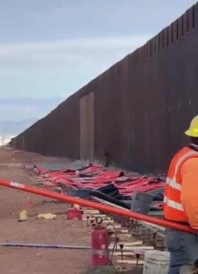 Man climbs the US-Mexico border while people are working on it