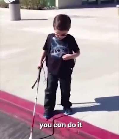 Blind kid experience his first curb by himself while his parents encouraged him.