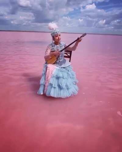 kazakh woman playing on traditional instrument... in the middle of a pink lake