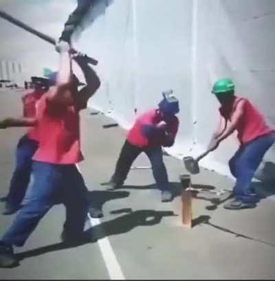 Synchronicity in action as four men pound an iron rod into the ground.