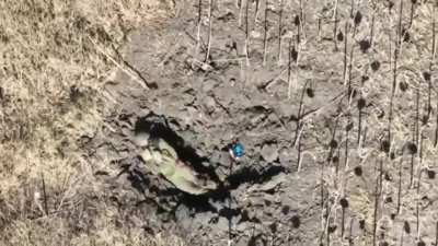 A Russian soldier, laying in a crater, is given a shock when targeted by a FPV drone that fails to detonate.