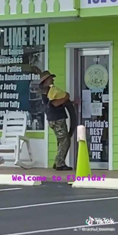 only in florida you can find an alligator with a t-shirt being held like a human baby