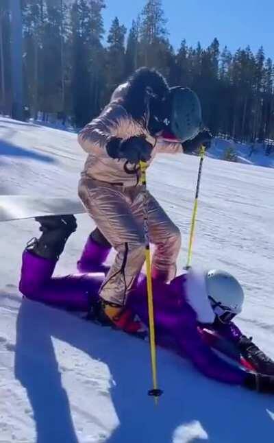 Snowboarding between a Skiers legs to provide a seat