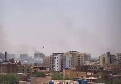 Sudanese Jet flies over Kahrtoum while smoke rises in the background as battles between Police forces+Military and RSF intensifies.