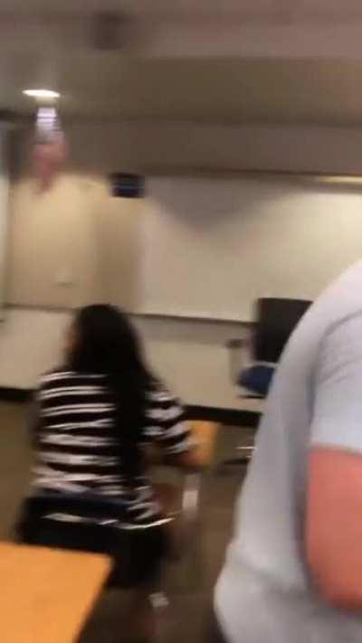 Girl cuts though classroom on a skateboard... good natured teacher laughs along with students