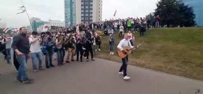 Peaceful Belarusian protesters are singing and dancing while the riot police in full body armor are blocking the street