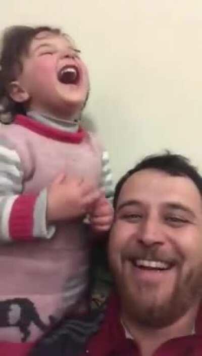 To distract his 4-year old daughter, her father has made up a game. Each time a bomb drops in Idlib Syria, they laugh, so she doesn’t get scared.