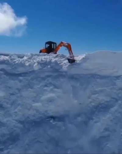 A dude on an excavator handles snow cornices