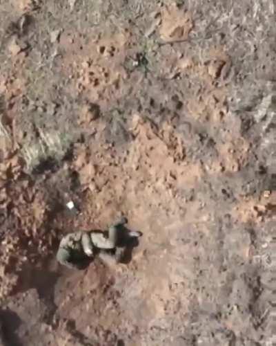 Russian soldier hiding in a shell crater has an M67 dropped on him by a Ukrainian drone