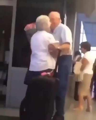 An older gentleman greeting his wife at the gate with flowers