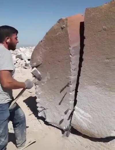 This man splitting a rock in half with a hammer and nails