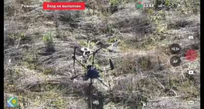 Drone footage of a Russian soldier retrieving a downed / crashed Ukrainian hexacopter, he uses a grappling hook and rope to remove the remaining TM-62M mine