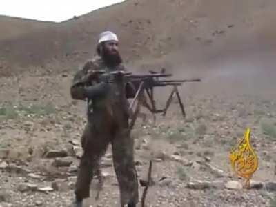 A Taliban fighter lifts two machine guns at once and fires them.