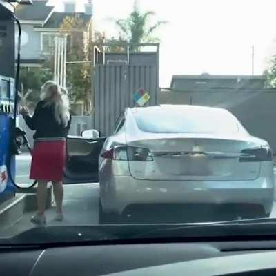 These guys having the time of their lives while a woman tries to figure out how to fill gas in her Tesla