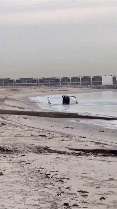 Main character driving his vehicle next to the shore flips his vehicle and falls out.