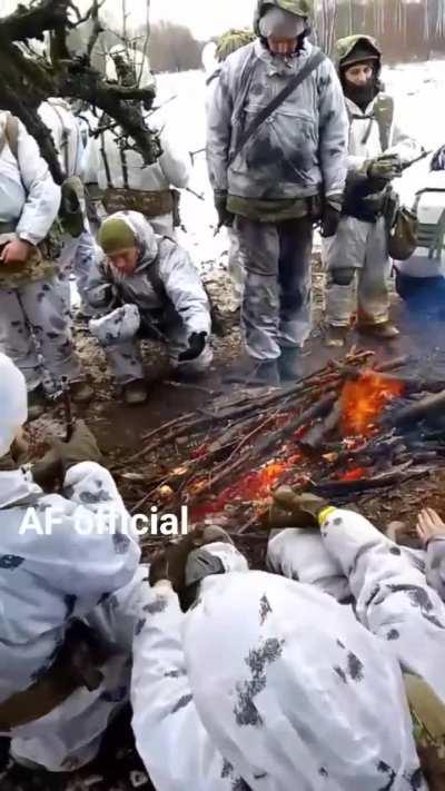 Ukrainian troops in snow camouflage warm themselves by the fire.