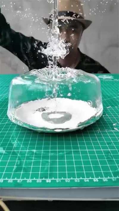 This man drops a metal ring onto a plate of water, creating a water cake.