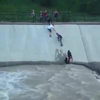 Drowning dog is saved by a group of madlads forming a human chain.