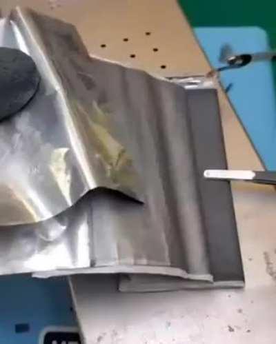 Professional cell phone repairer opens up a bloated Samsung battery, showing what's inside