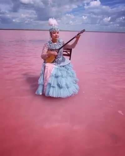 kazakh woman playing on traditional instrument... in the middle of a pink lake