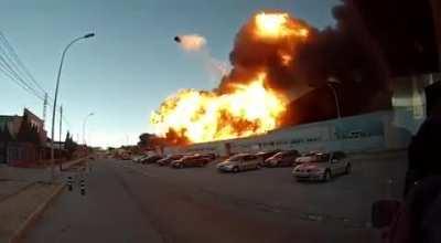 Burning warehouse explodes, sending a propane tank flying high.