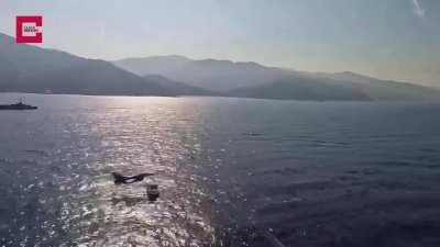 Turkish Air Force F-16 fighter jet passing at extremely low altitude over a ship at the sea.