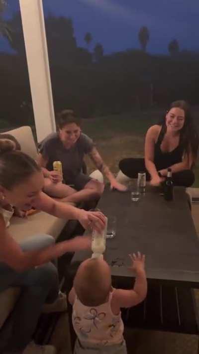 Baby chugging milk with some encouragement from his/her aunties