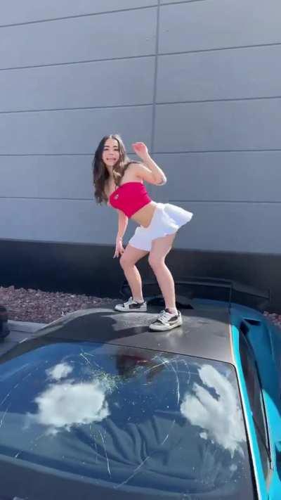 A girl climbs and dances on a expensive car 