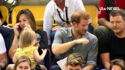 Mother realising her toddler is stealing popcorn from an unaware Prince Harry